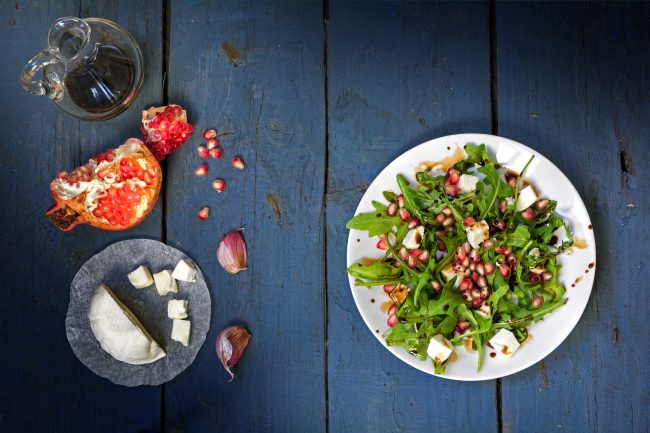 rocket salad with cheese and pomegranate on rustic wood, view fr